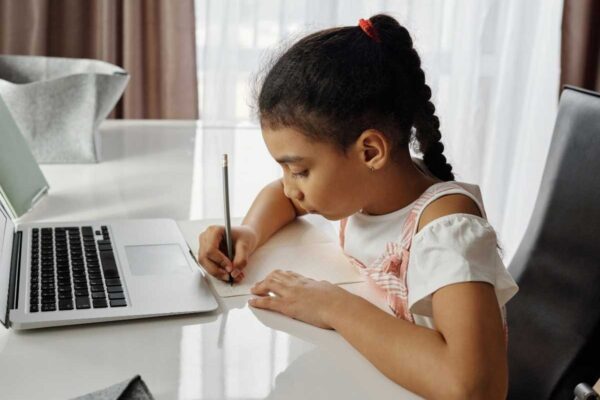 Child writing while working on laptop